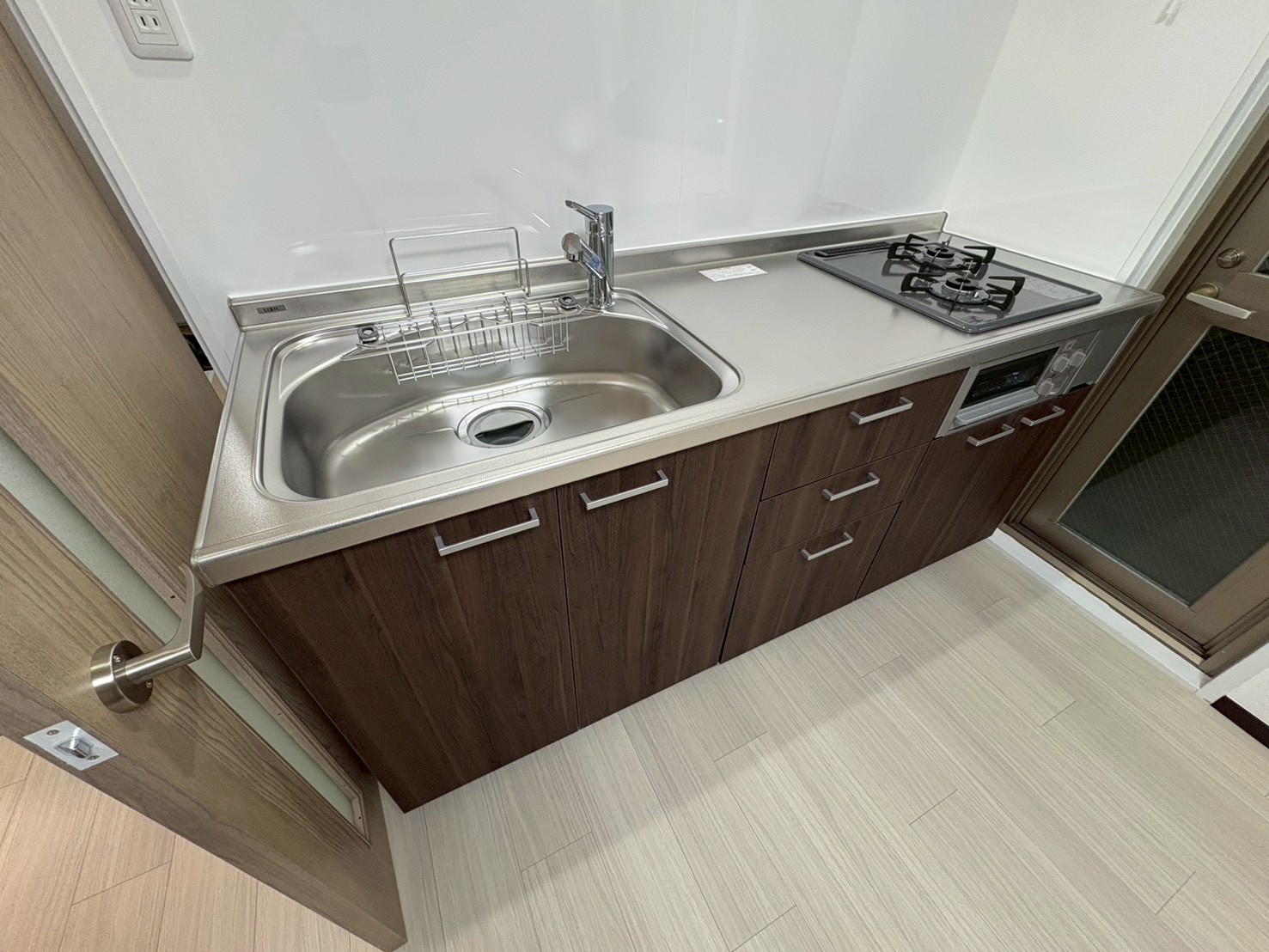 落ち着いたダークブラウンのキャビネットと、3口コンロを備えたシステムキッチン。